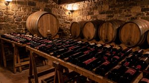 Rangées de bouteilles de vin rouge dans une cave traditionnelle aux murs de pierre, éclairées par une lumière chaude et sobre.