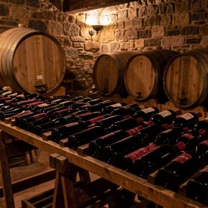 Rangées de bouteilles de vin rouge dans une cave traditionnelle aux murs de pierre, éclairées par une lumière chaude et sobre.